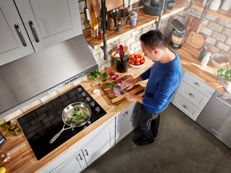 A person chopping vegetables next to their glass cooktop