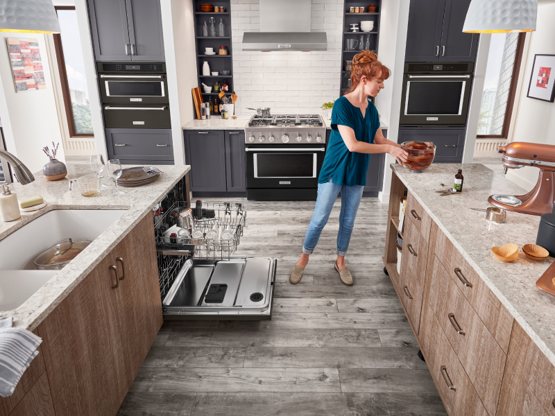 A KitchenAid® stand mixer on the counter with a person about to place the stand mixer bowl in the dishwasher.