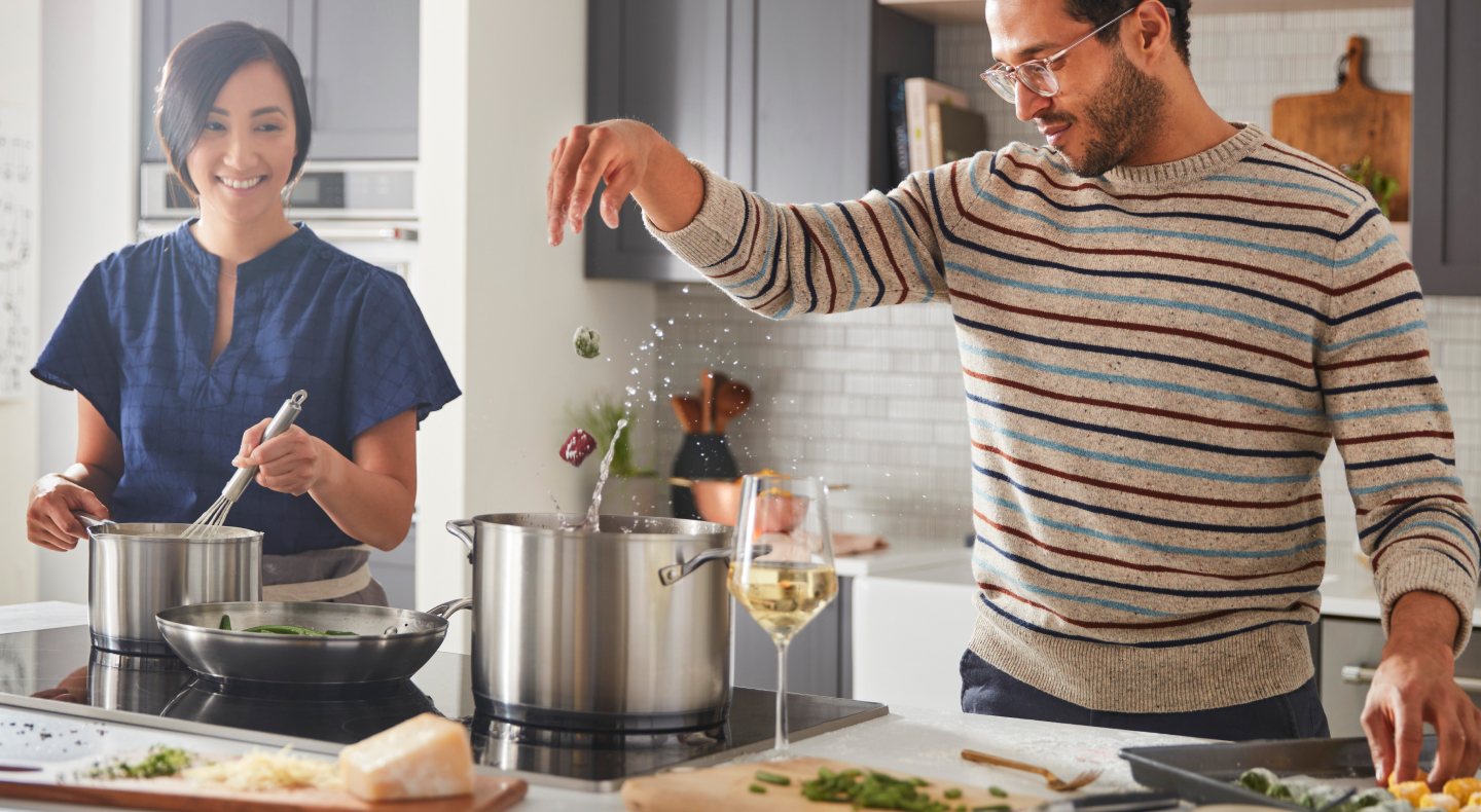 A man and woman preparing various dishes with a cooktop