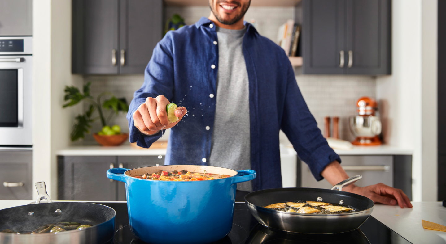 A man squeezing lime into a dish on a cooktop