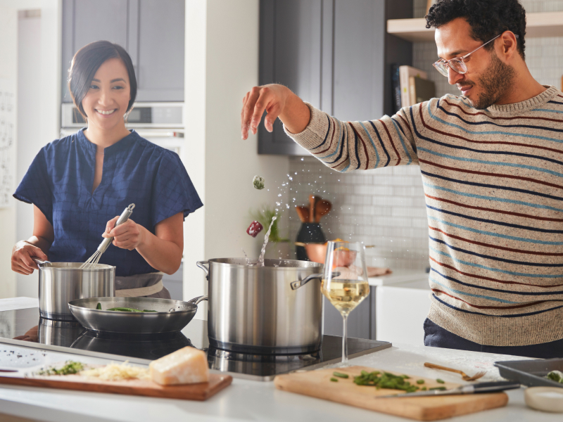A man and woman preparing various dishes with a cooktop