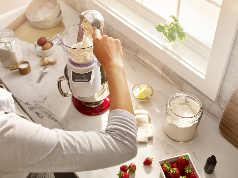 A person pouring flour into KitchenAid® Sifter & Scale Attachment.
