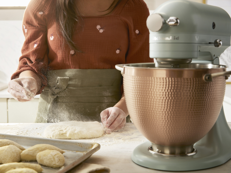 A person sprinkling dough with flour next to a KitchenAid® stand mixer.