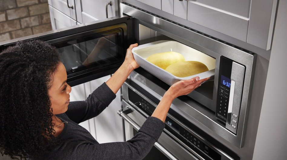 A person placing a dish with loaves of dough into a microwave to proof