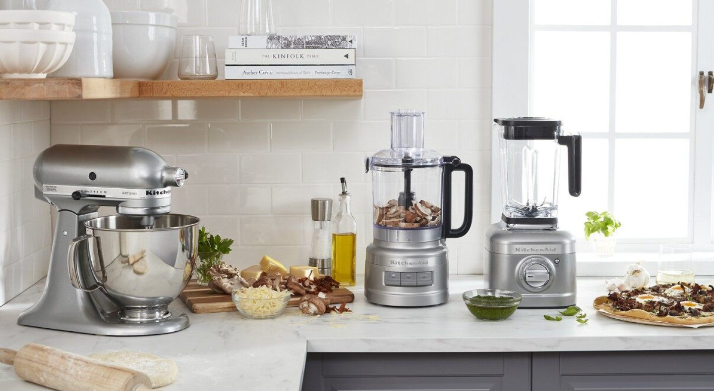 KitchenAid® stand mixer, food processor and blender on countertop with cutting board and ingredients