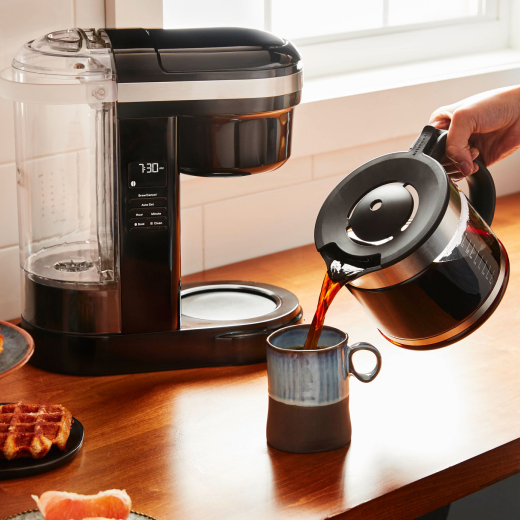 Person pouring coffee from a KitchenAid® Drip Coffee Maker into a ceramic mug 