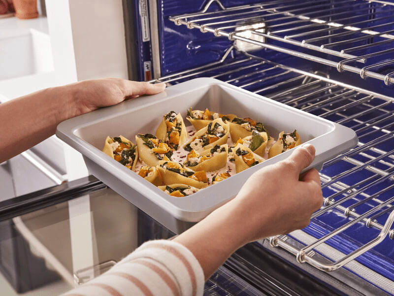 A person placing a tray of stuffed shells on the lower rack of a convection oven