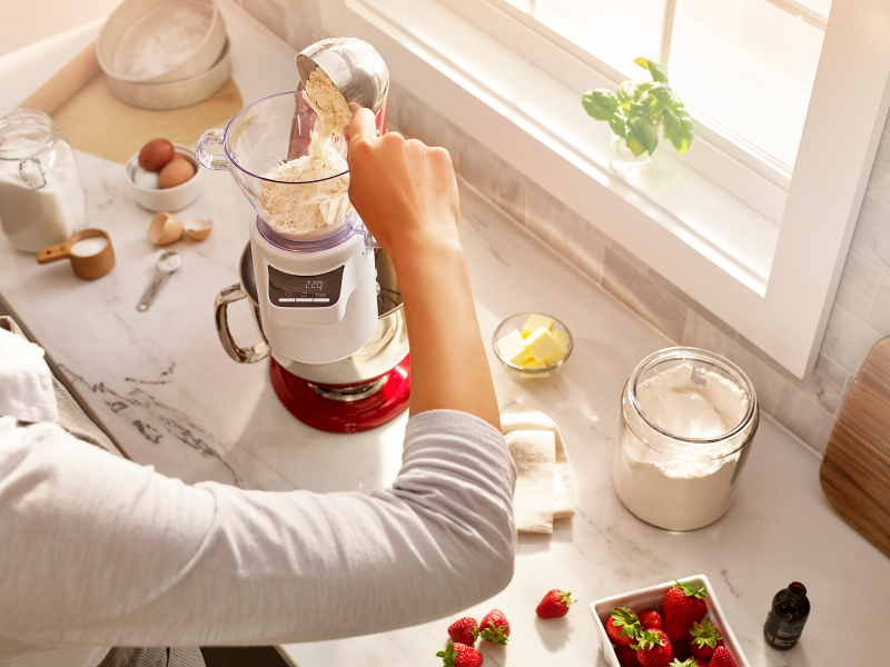 A person pouring flour into KitchenAid® Sifter & Scale Attachment.