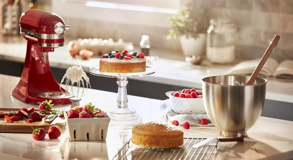 KitchenAid® stand mixer next to a cake, bowl of whipped cream and carton of berries.