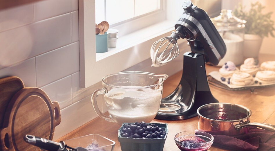 KitchenAid® stand mixer on countertop with whipped cream in a glass mixer bowl next to fresh berries.
