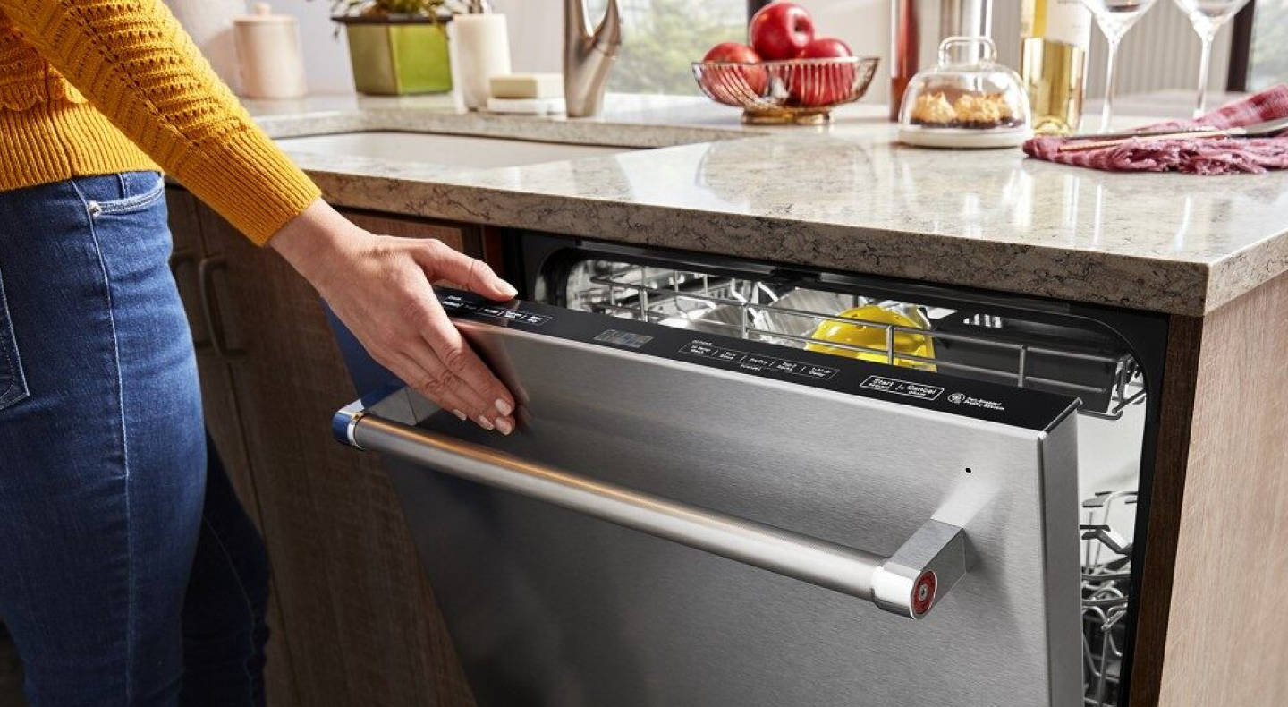 Person closing a stainless steel top control dishwasher