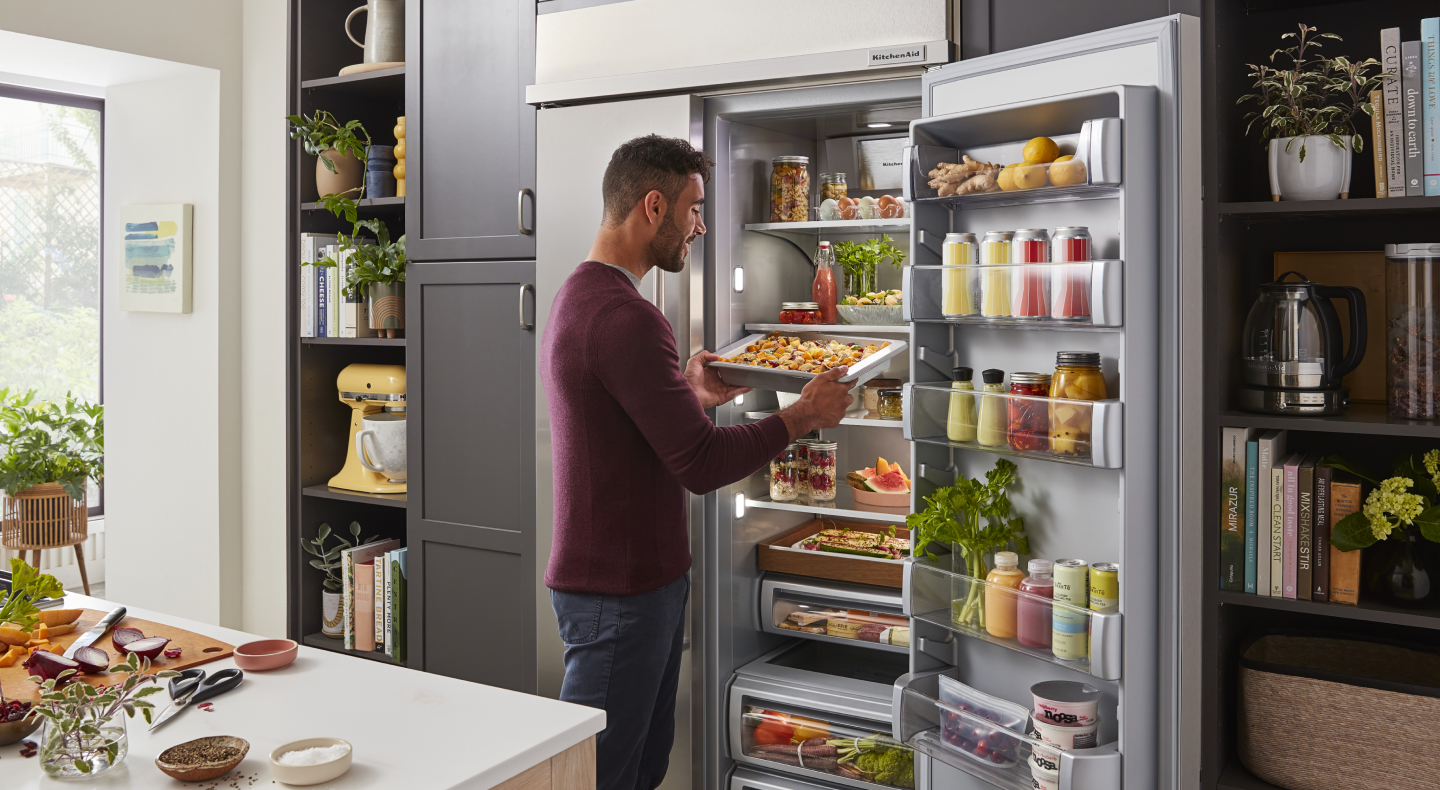 Person putting prepared baked goods in the refrigerator on a cookie sheet