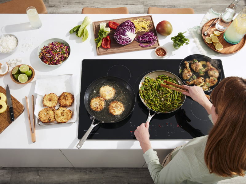 Person sauteeing green beans on electric cooktop surrounded by ingredients