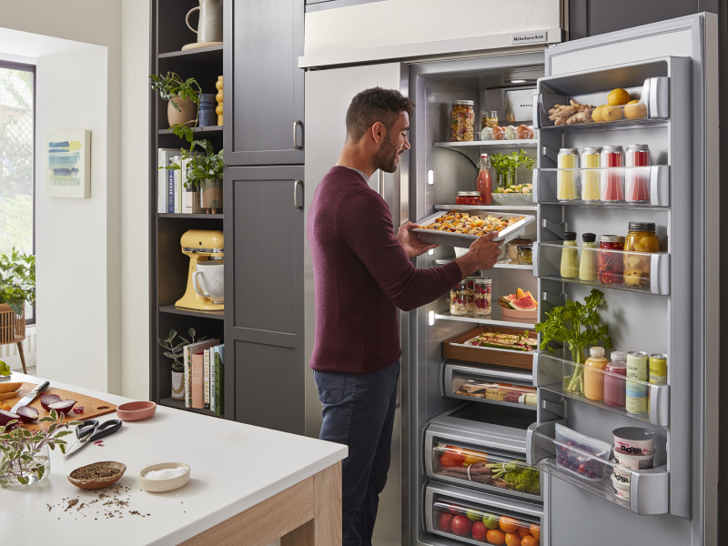 Person putting prepared baked goods in the refrigerator on a cookie sheet