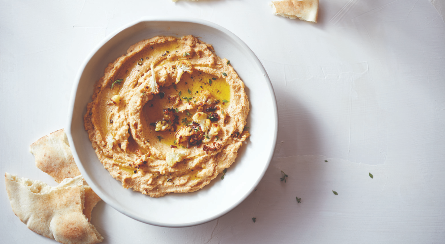 Hummus topped with herbs next to slices of pita bread