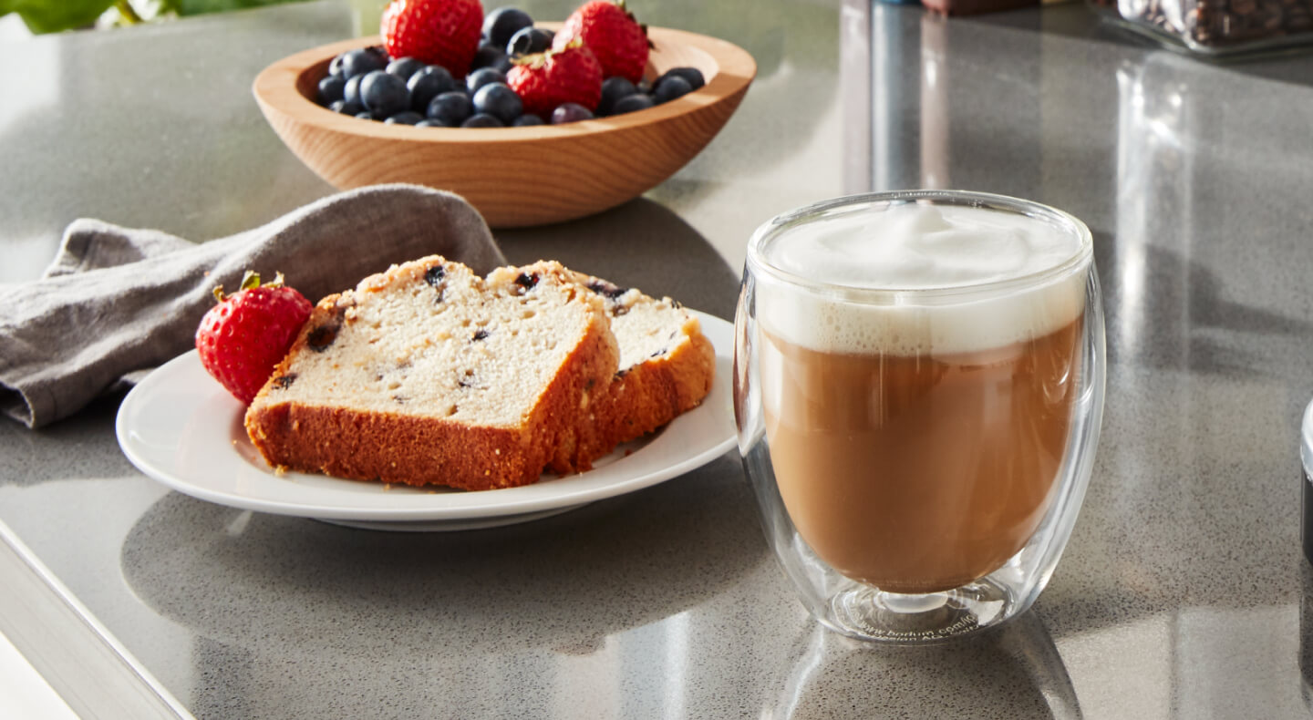 Espresso drink on counter with slices of bread and fruit