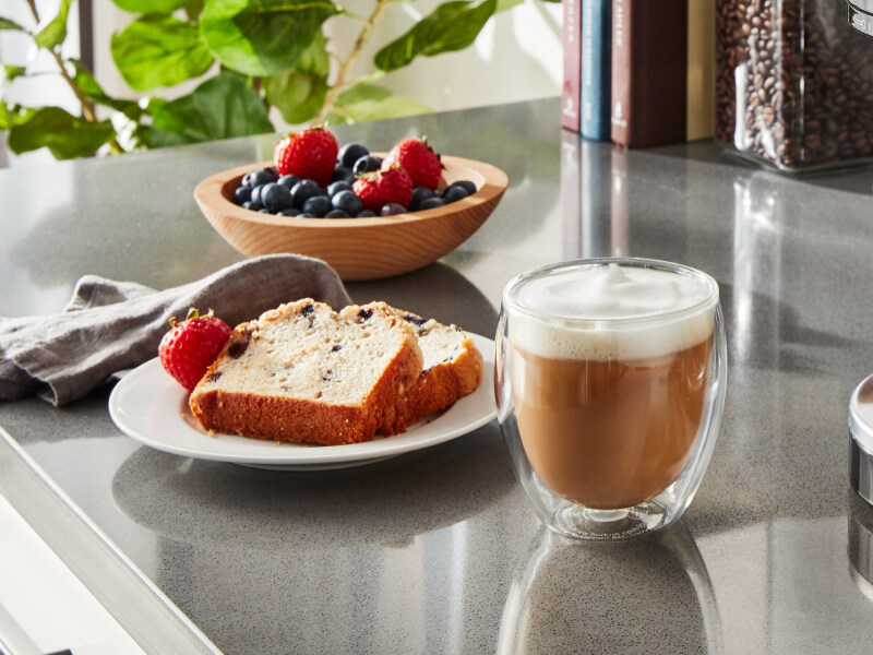 Espresso drink on counter with slices of bread and fruit