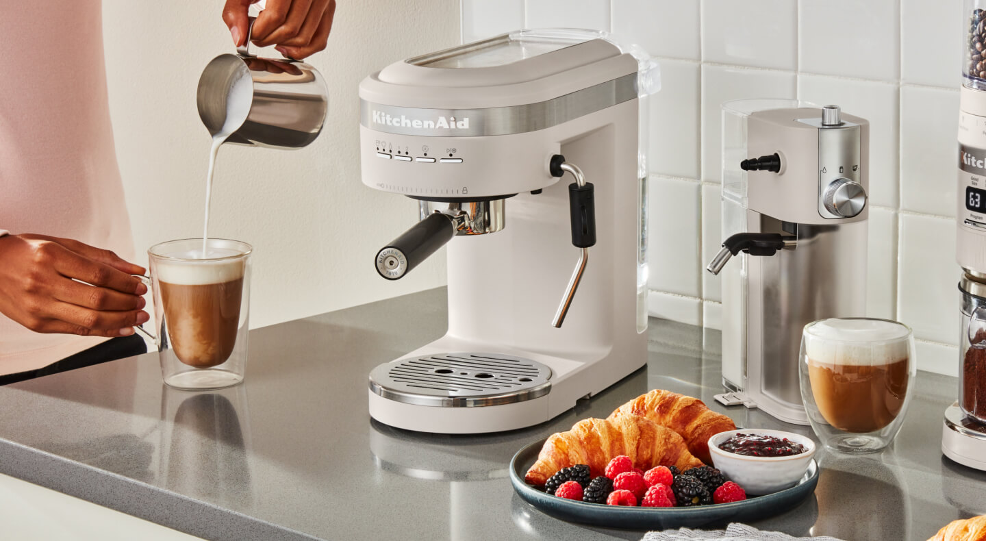 Person pouring frothed milk into an espresso drink next to an semi-automatic type of espresso machine