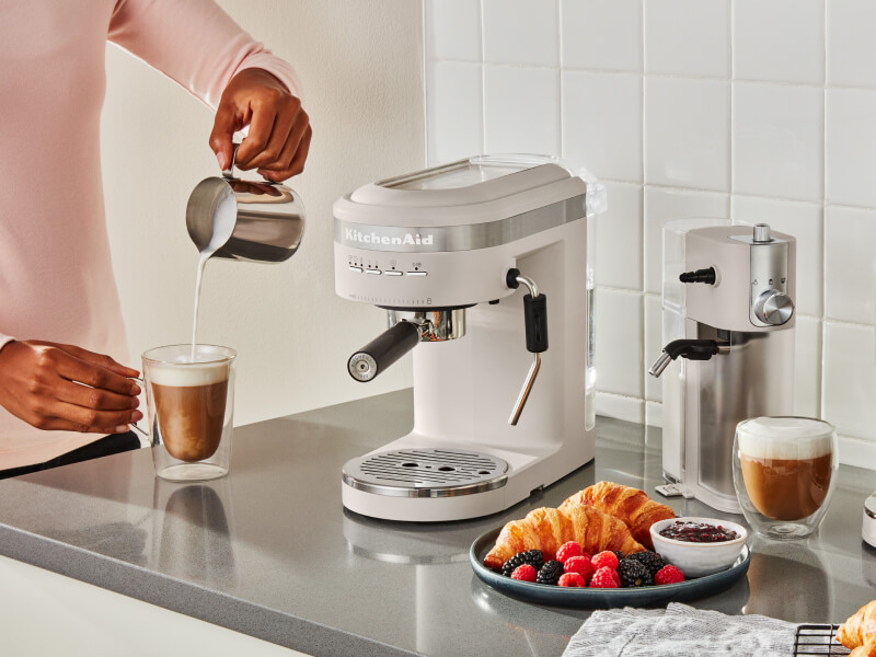 Person pouring frothed milk into an espresso drink next to an semi-automatic type of espresso machine