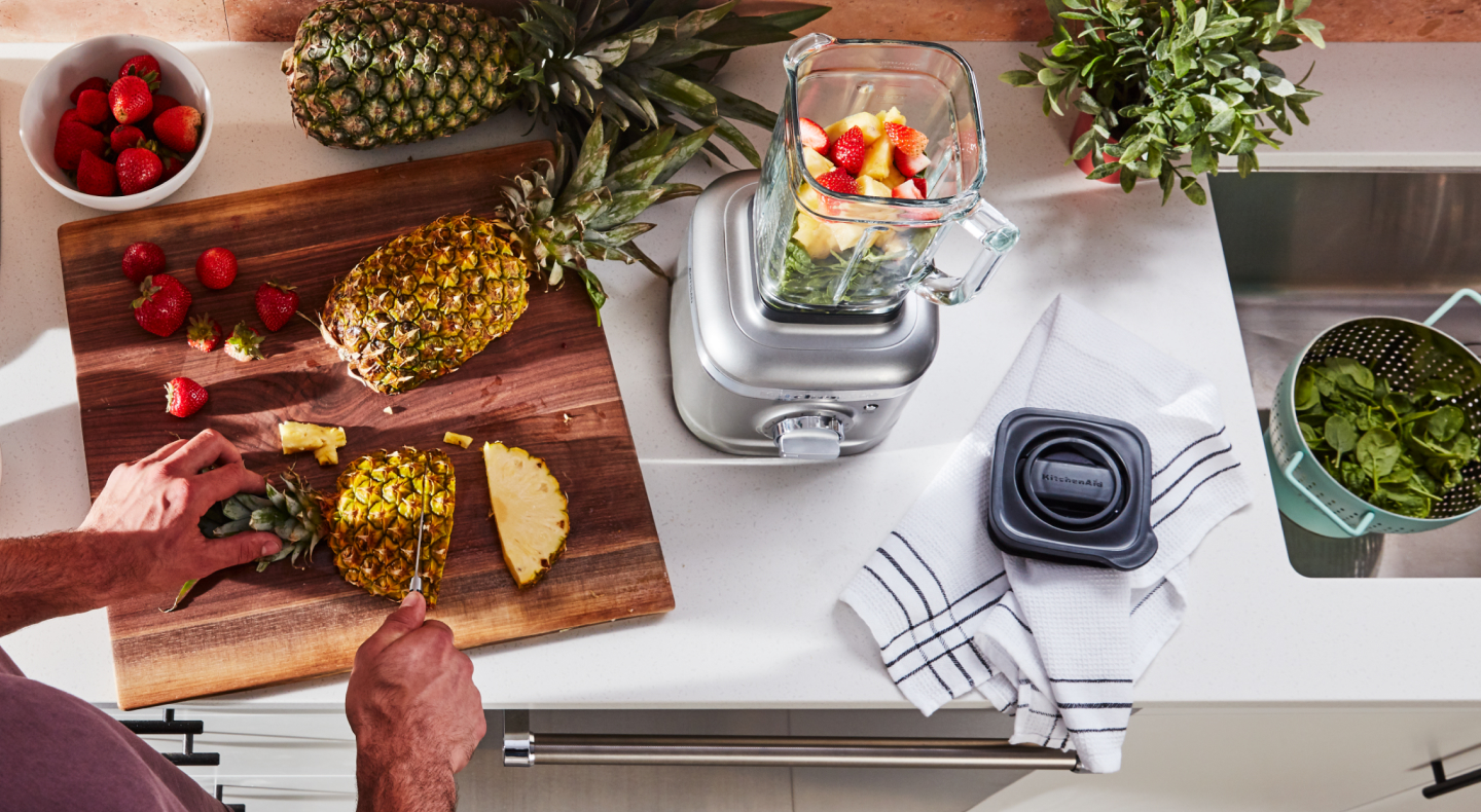 Person cutting pineapple next to a KitchenAid® blender