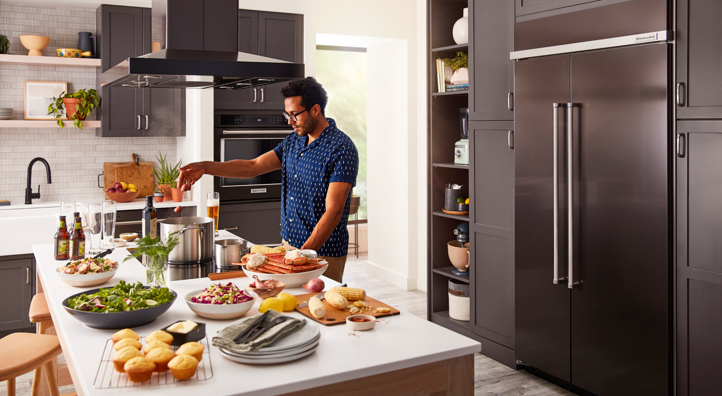 Person cooking at an island in front of a built-in, black stainless steel KitchenAid® side-by-side refrigerator