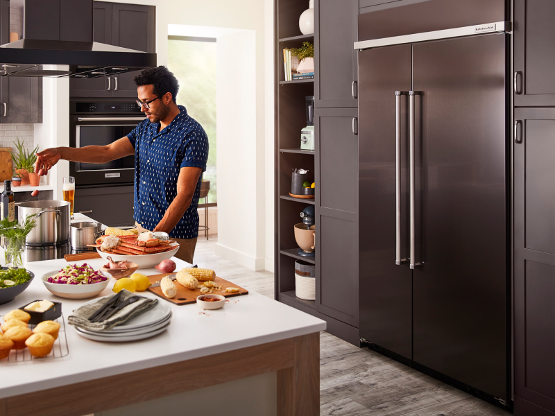 Person cooking at an island in front of a built-in, black stainless steel KitchenAid® side-by-side refrigerator