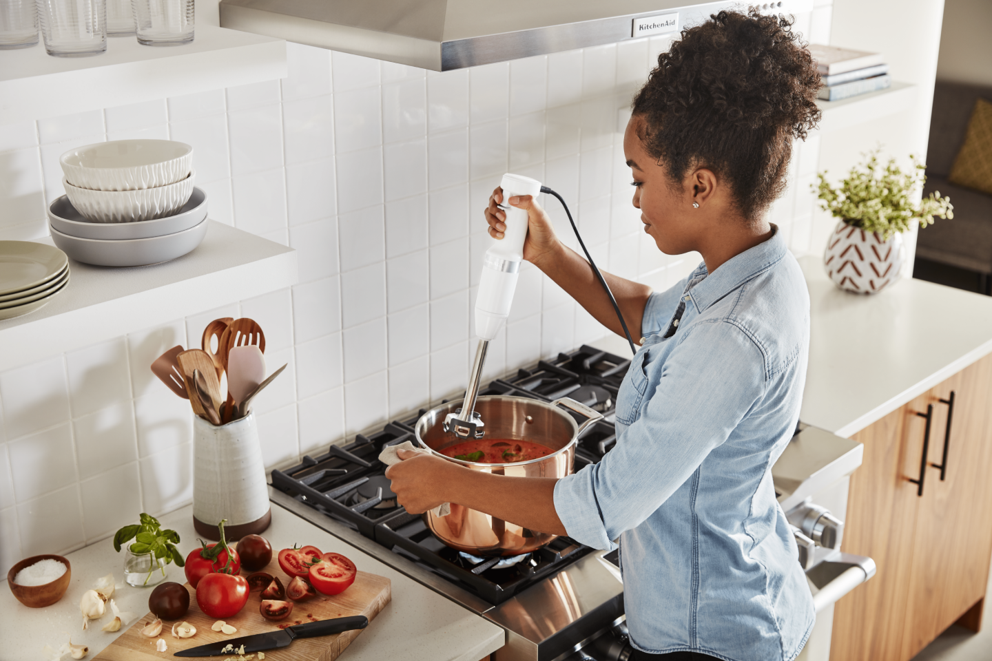 Maker using KitchenAid® immersion blender to mix ingredients in pot on top of stovetop