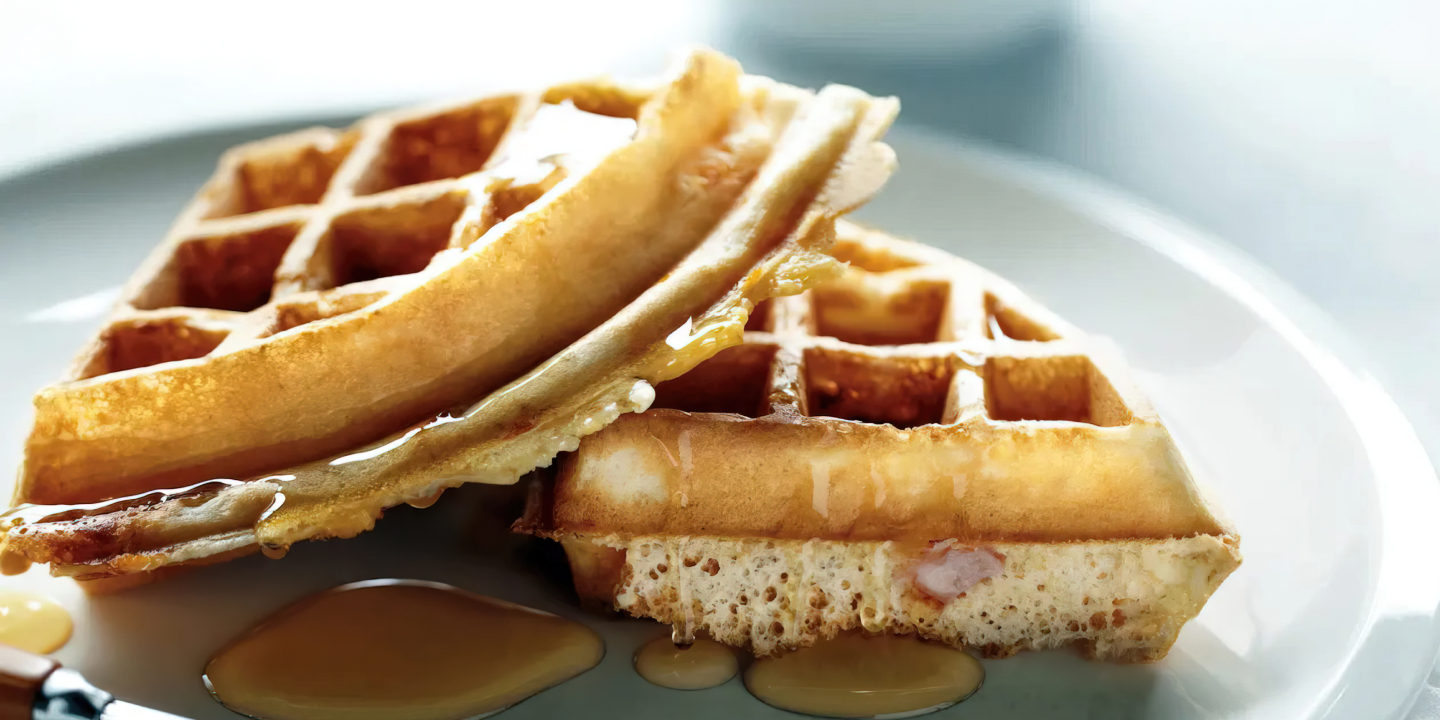 Two quarters of waffles sitting on a plate, drizzled with syrup. 