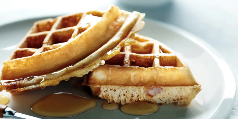 Two quarters of waffles sitting on a plate, drizzled with syrup. 