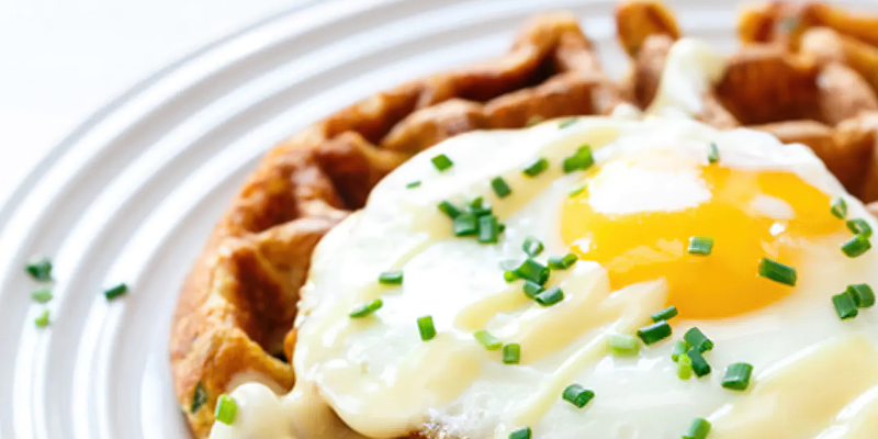 A waffle sitting on a plate, topped with a fried egg and chives.