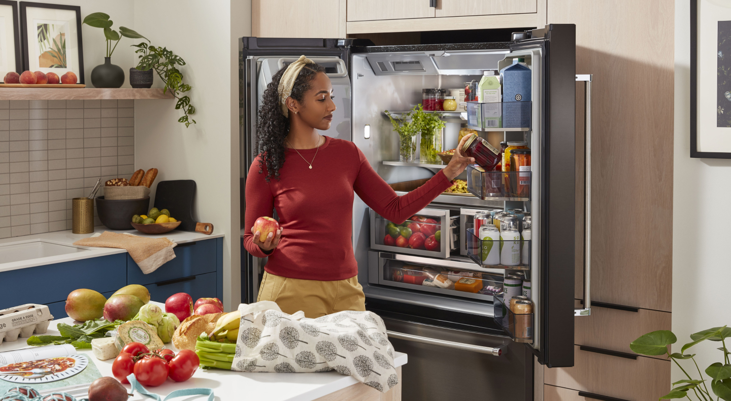 Person putting items in a KitchenAid® French door refrigerator near ingredients on counter