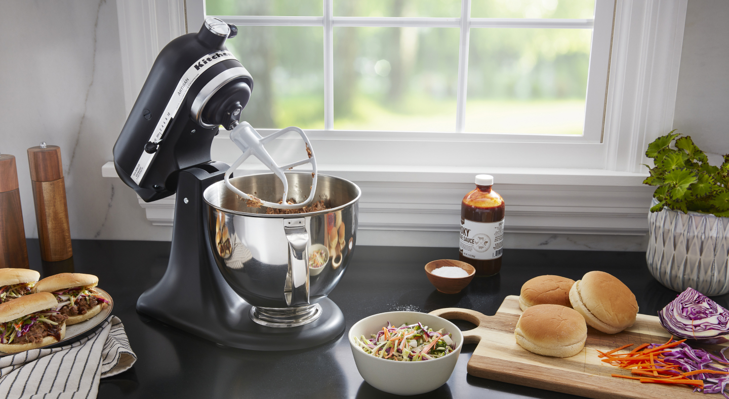 A black tilt-head KitchenAid® stand mixer mixing meat