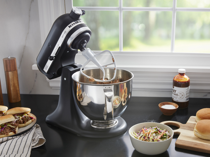 A black tilt-head KitchenAid® stand mixer mixing meat
