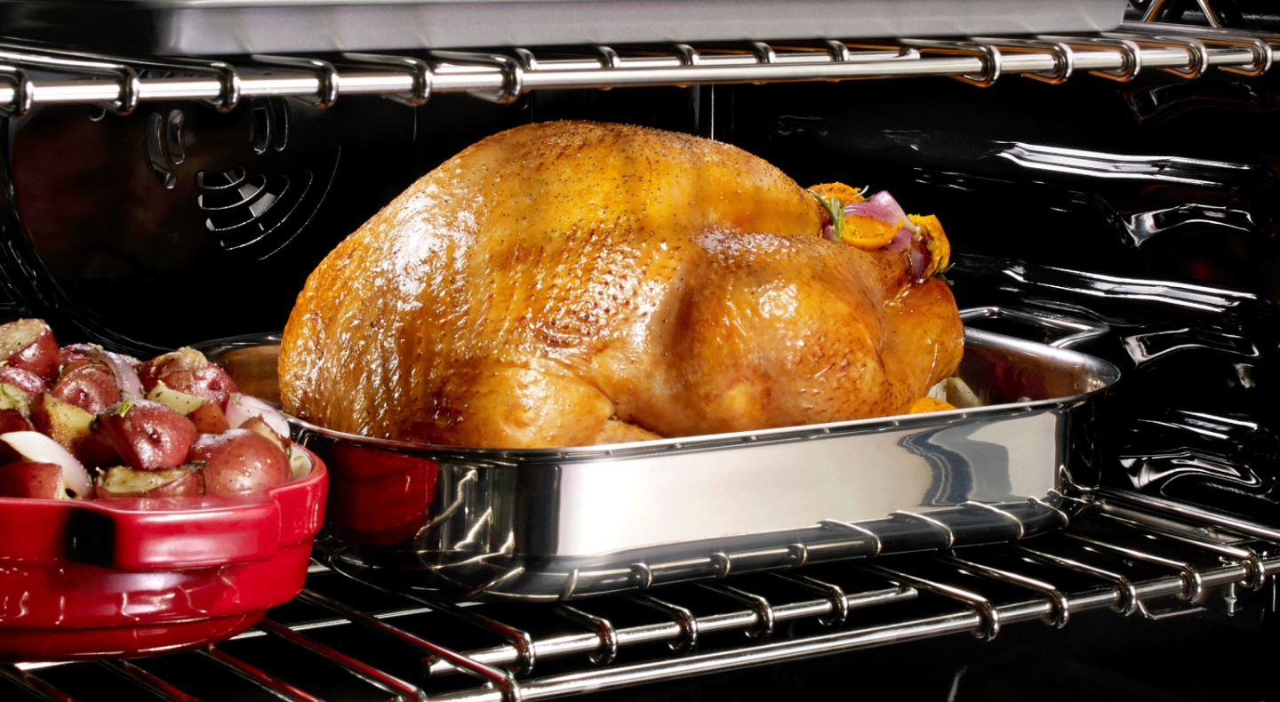 Turkey in an oven next to a casserole dish of red potatoes