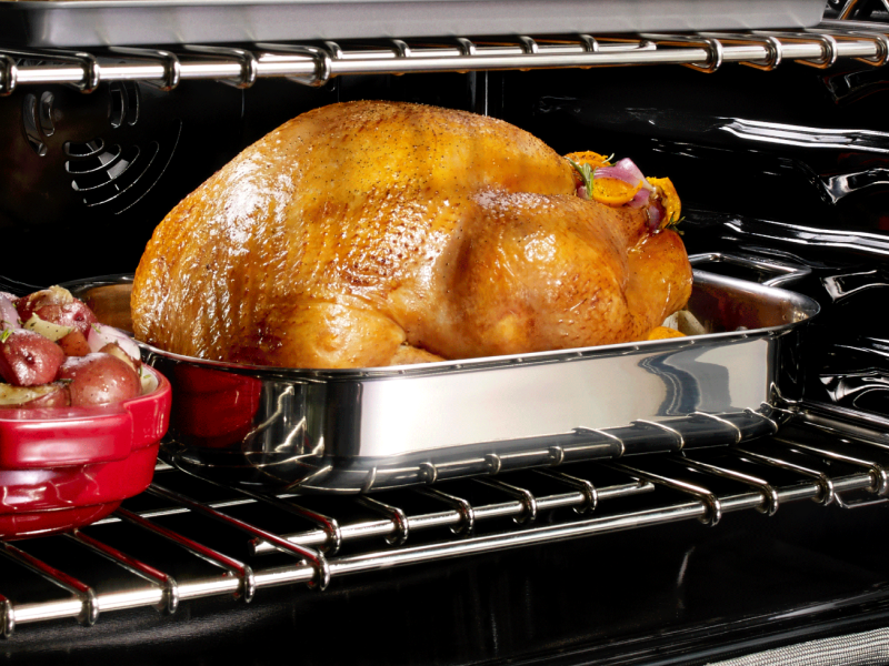 Turkey in an oven next to a casserole dish of red potatoes