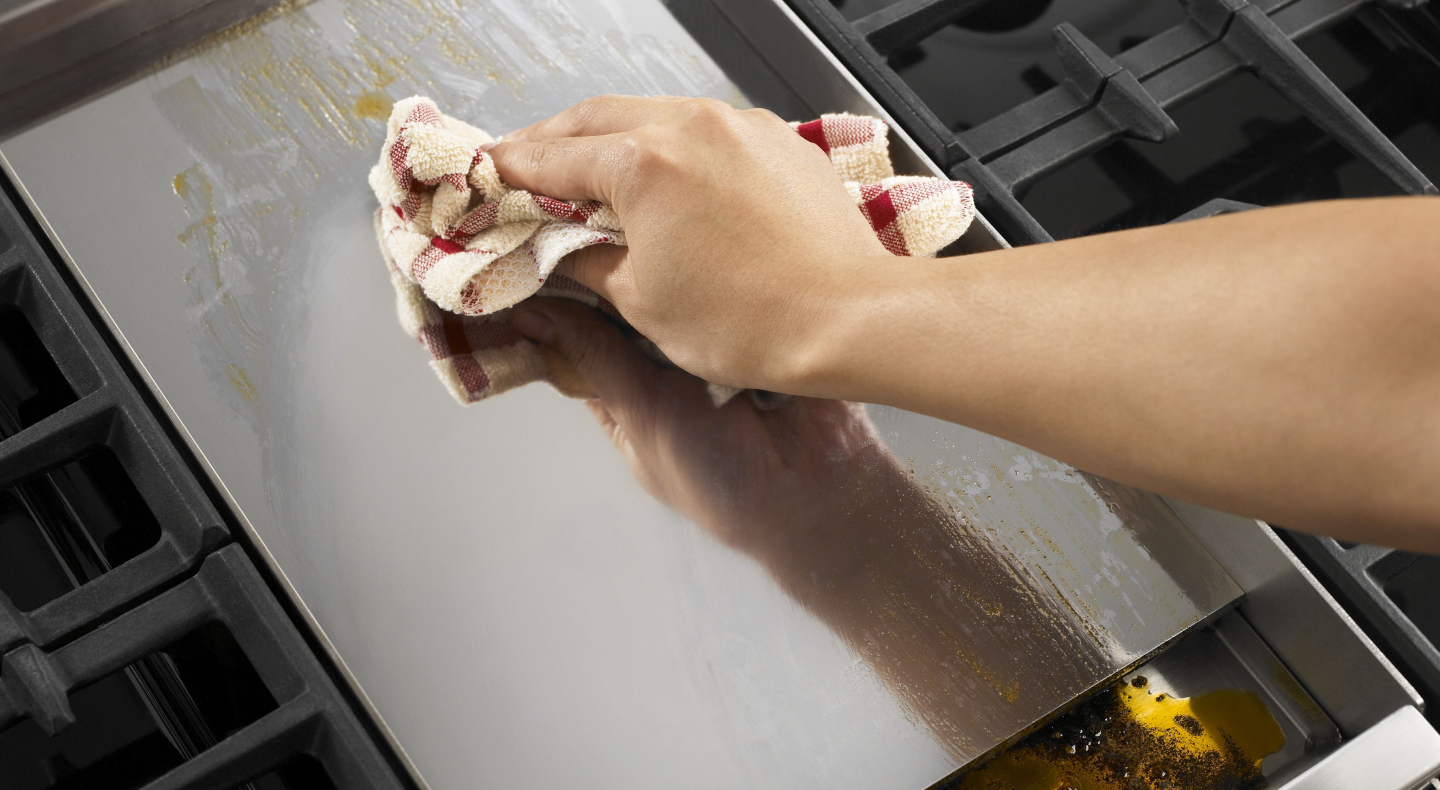 Person wiping griddle with clean dish rag