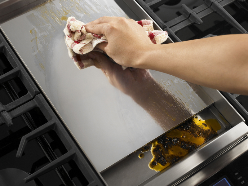 Person wiping griddle with clean dish rag