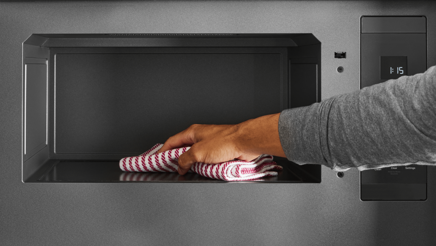 Person using a cloth to clean the interior of a microwave