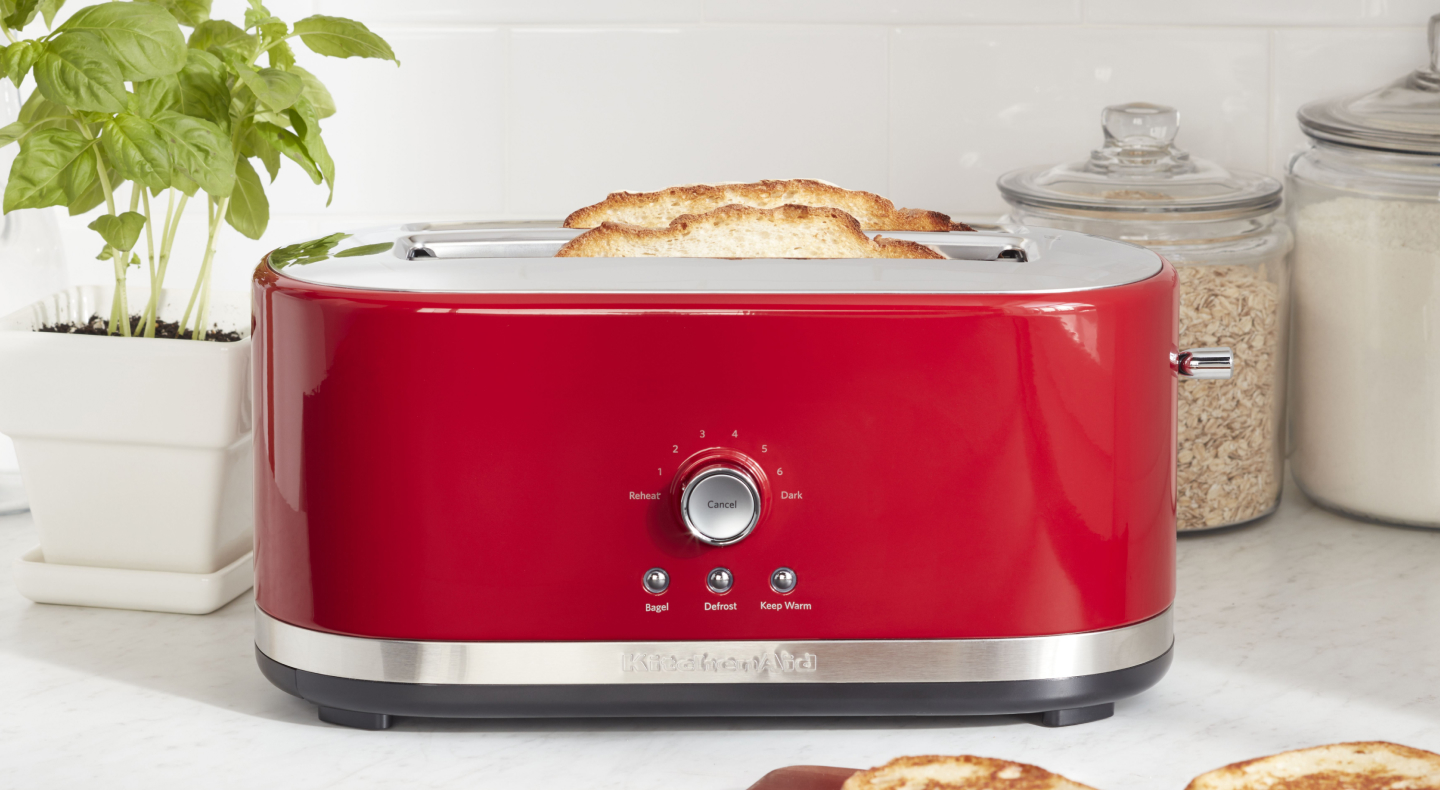 Slices of bread in a red KitchenAid® toaster on a modern kitchen counter.