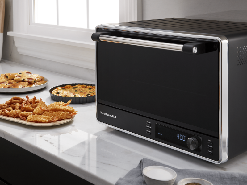 A black KitchenAid® air fryer and various appetizers on a countertop