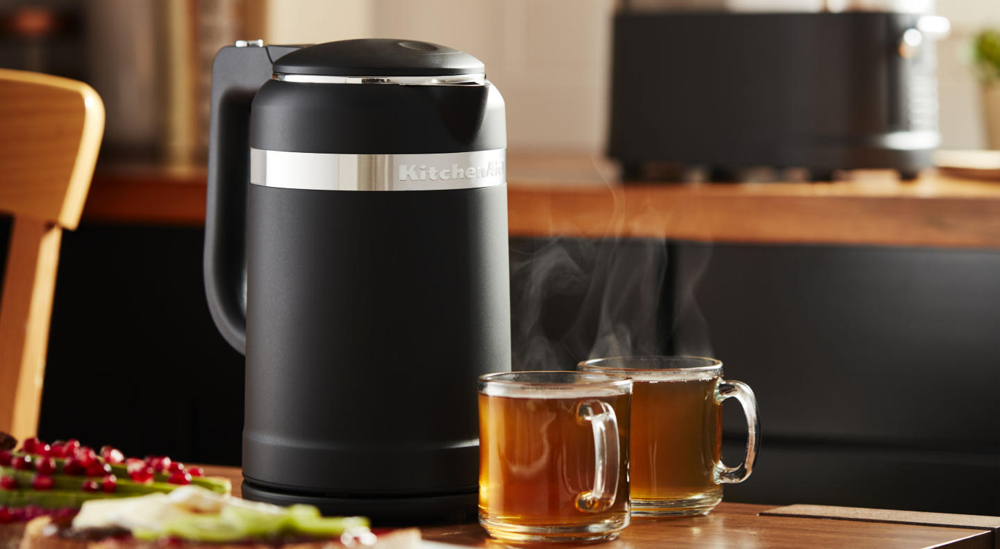 Black electric tea kettle on a countertop next to full glasses of tea