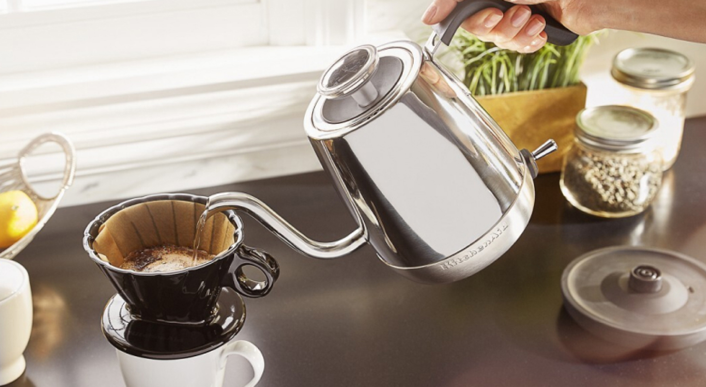 A woman pouring hot water from a KitchenAid® electric kettle into a pour-over coffee  mug
