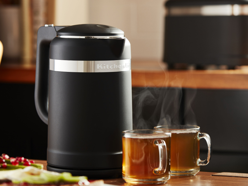 Black electric tea kettle on a countertop next to full glasses of tea