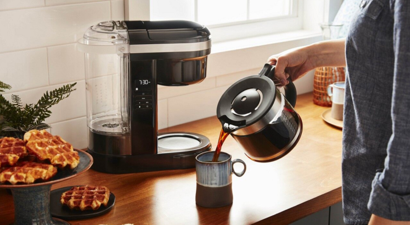 Woman pouring coffee into a mug with drip coffee maker in background