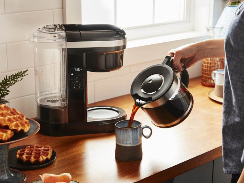 Woman pouring coffee into a mug with drip coffee maker in background