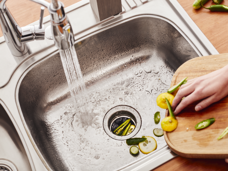Person scraping vegetable scraps into a stainless steel sink