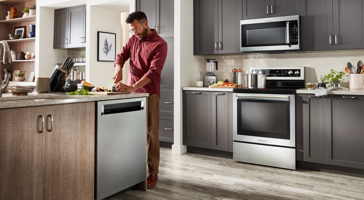 Person chopping veggies in a kitchen with a suite of KitchenAid® appliances 