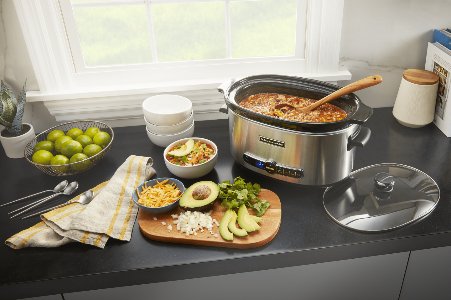 KitchenAid® slow cooker filled with chili next to a cutting board of vegetables and herbs