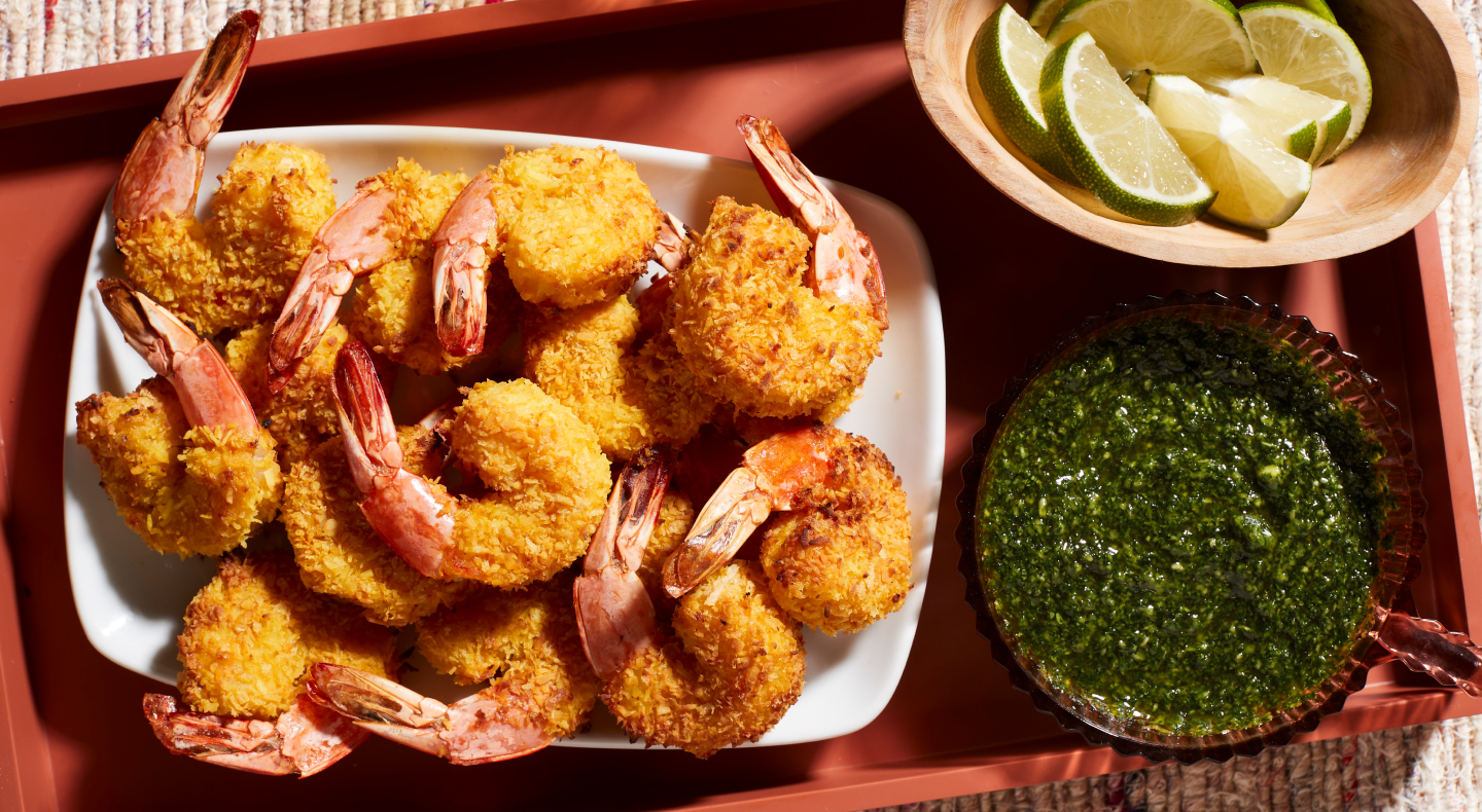 A closeup of air fryer shrimp on a serving tray next to a fresh sauce and lime slices.