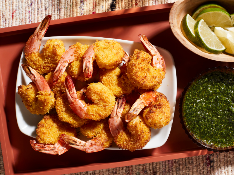 A closeup of air fryer shrimp on a serving tray next to a fresh sauce and lime slices.